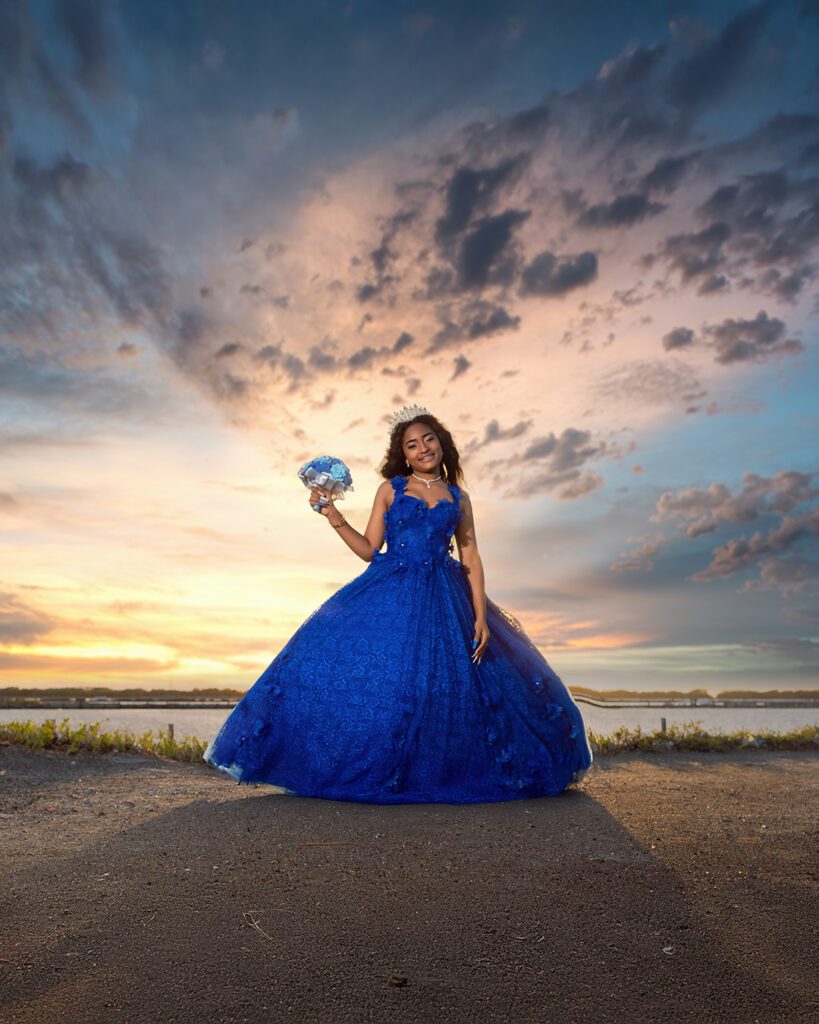 Quinceañera con vestido azul real posando al atardecer en paisaje natural. Fotografía de 15 años en locaciones del sur (Dunas/Salinas).